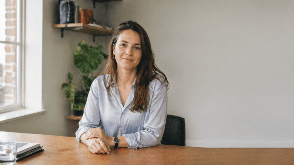 Vriendelijke vrouw zit aan een bureau en kijkt uitnodigend in de camera